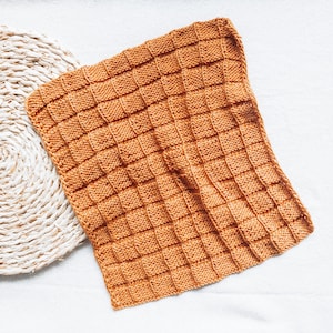 May include: A knitted throw blanket in a warm orange color. The blanket has a textured, waffle-like pattern.