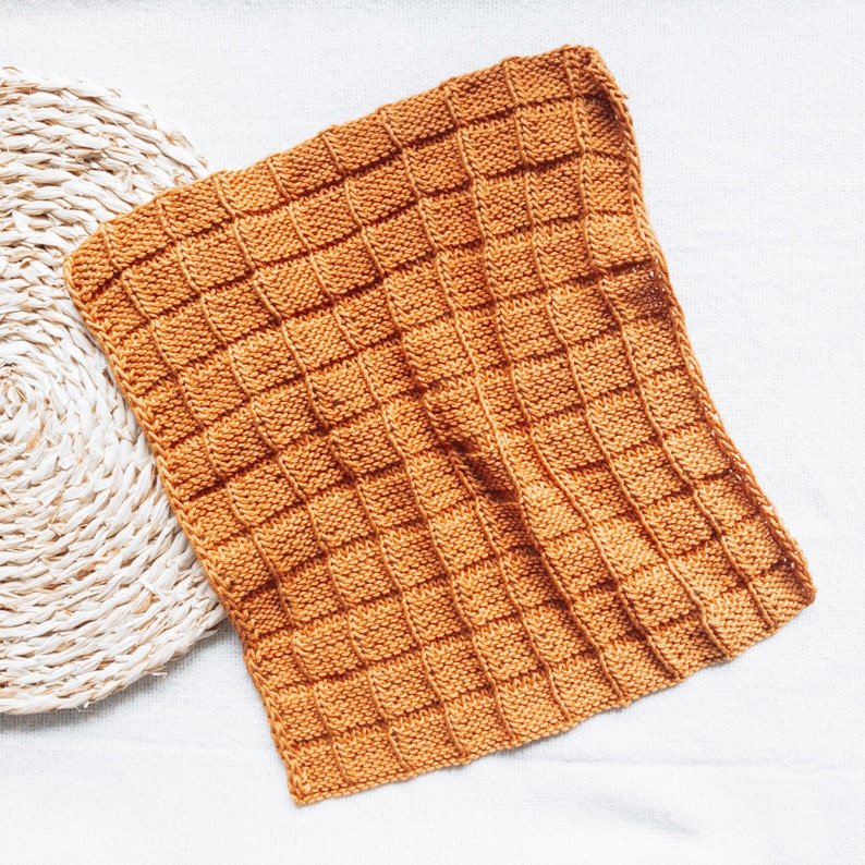May include: A knitted throw blanket in a warm orange color. The blanket has a textured, waffle-like pattern.