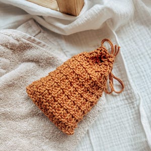 May include: A small, brown knitted pouch with a drawstring closure. The pouch is made of a soft, textured yarn and has a rustic, handmade look.