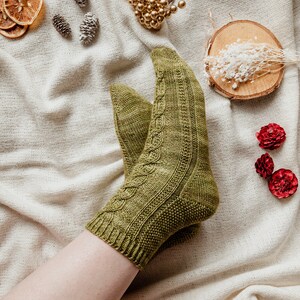 May include: A pair of green knitted socks with a cable knit pattern. The socks are worn on a person's foot and leg.