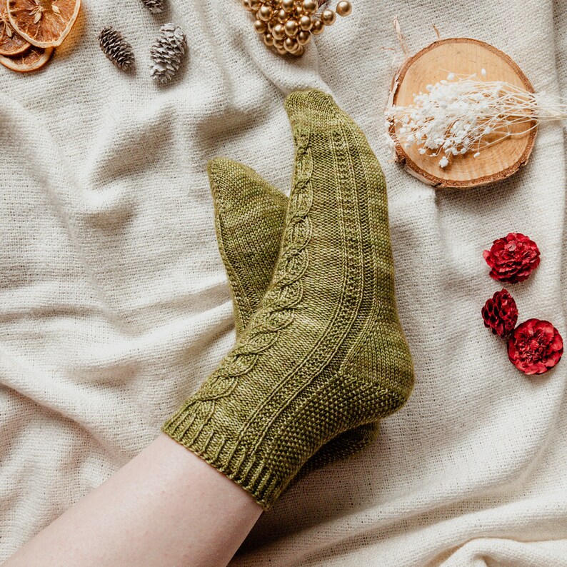 May include: A pair of green knitted socks with a cable knit pattern. The socks are worn on a person's foot and leg.