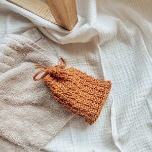 May include: A brown crocheted pouch with a drawstring closure. The pouch is sitting on a white towel.