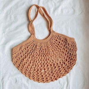 Peut inclure: Un sac fourre-tout en maille ouverte de couleur beige avec deux anses tress&eacute;es. Le sac a un fond arrondi et un design en forme de filet, id&eacute;al pour transporter des courses ou d'autres articles. Le sac est fait d'une fibre naturelle et douce.