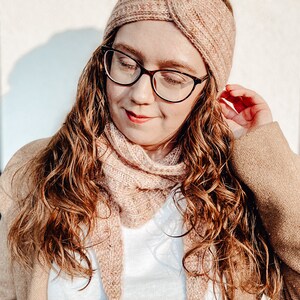 May include: A woman wearing a pink knitted headband and matching scarf. The headband is knotted on top of her head and the scarf is draped around her neck.