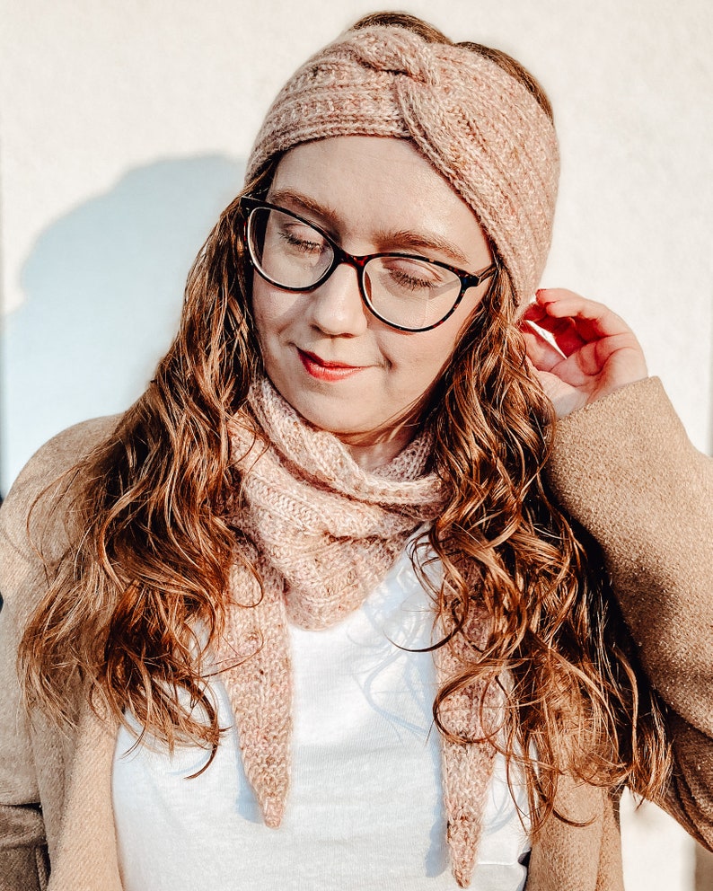 May include: A woman wearing a pink knitted headband and matching scarf. The headband is knotted on top of her head and the scarf is draped around her neck.