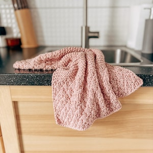 May include: A pink knitted dishcloth hangs over the edge of a kitchen counter.