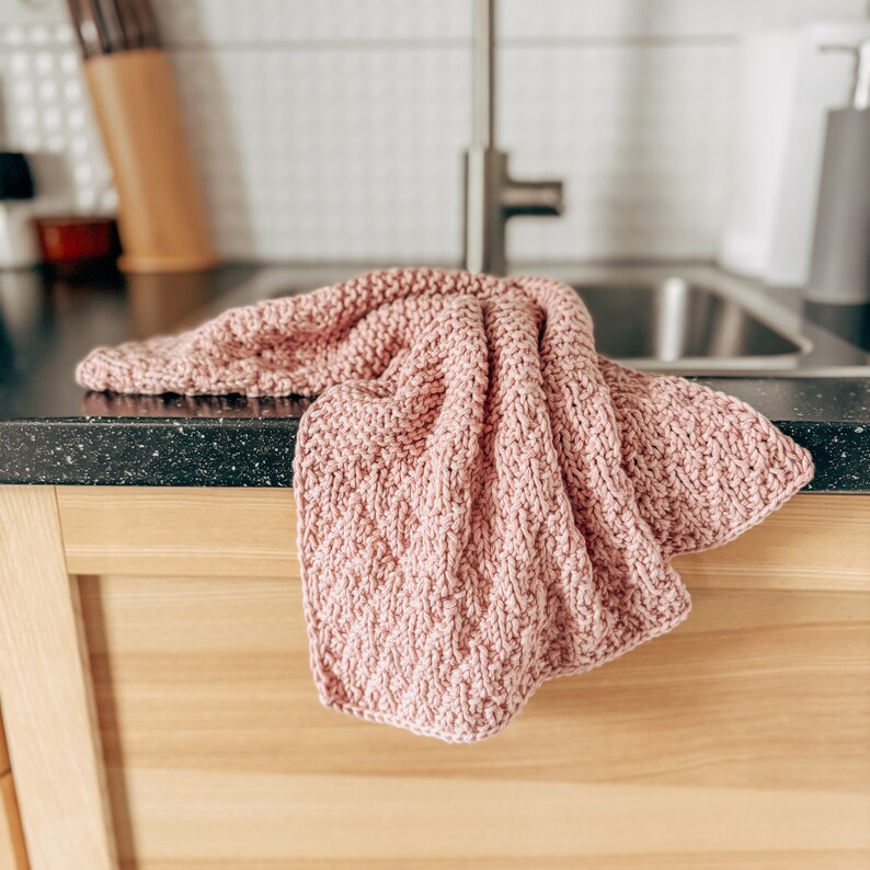 May include: A pink knitted dishcloth hangs over the edge of a kitchen counter.