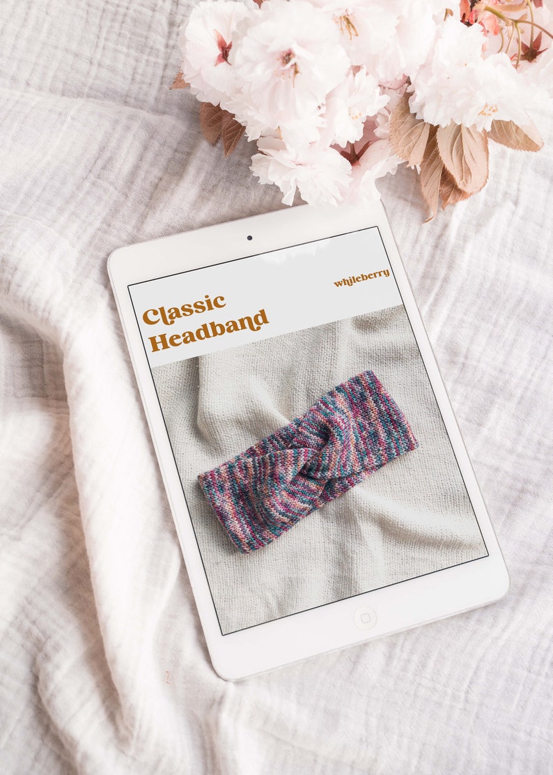 May include: A digital tablet displaying a knitting pattern for a classic headband. The pattern is titled "Classic Headband" and the designer is "whileberry". The headband is a colorful, multi-colored knit with a knot in the center.