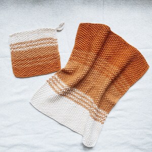 May include: Two knitted dishcloths in a gradient of orange and white. The dishcloths are made with a textured stitch and have a subtle ombre effect.