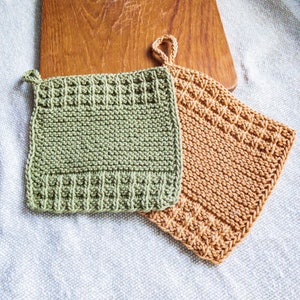 May include: Two knitted pot holders, one green and one brown, with hanging loops. The pot holders are made of a textured yarn and have a square shape.
