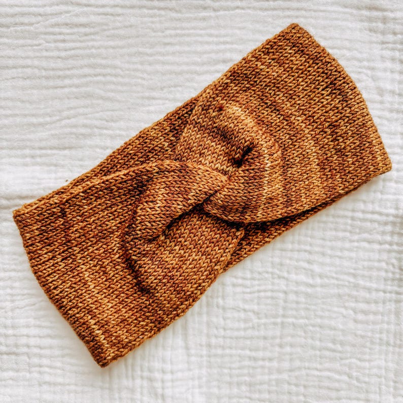 May include: A brown knitted headband with a twisted knot design.