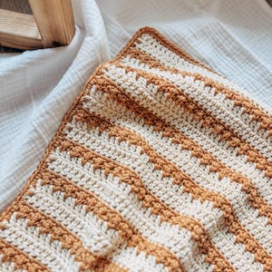May include: A crocheted baby blanket with a striped pattern in cream and mustard yellow.