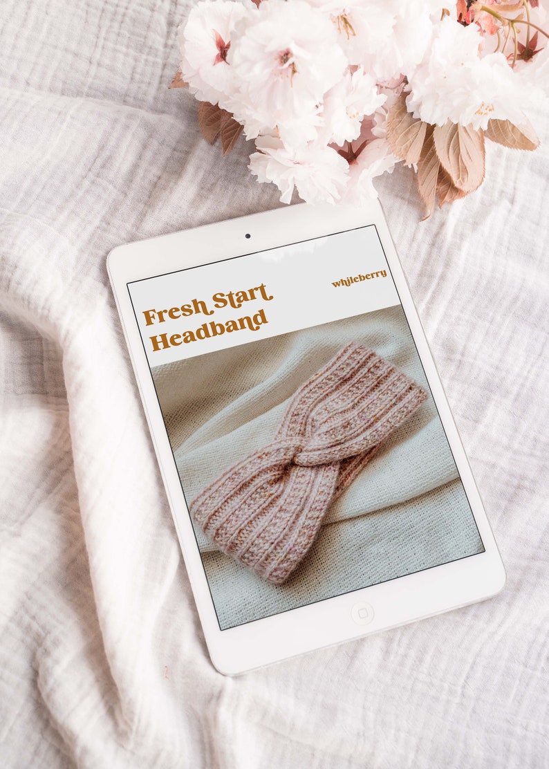 May include: A digital tablet displaying a knitting pattern for a pink headband titled "Fresh Start Headband" by "whistleberry".