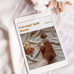 Puede incluir: Una tableta digital que muestra un patr&oacute;n de tejido para "Caramel Spill Socks" de "whileberry". El patr&oacute;n presenta un primer plano de calcetines rayados marrones sobre un fondo blanco con rodajas de naranja secas y pi&ntilde;as.