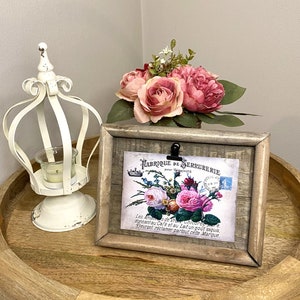 Op de afbeelding: Een rustiek houten fotolijst met een witte achtergrond en een vintage bloemenprint. De print toont een boeket roze rozen en de tekst "FABRIQUE DE SERRURERIE" met een Frans geïnspireerd ontwerp.