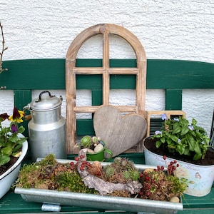 May include: A decorative wooden arched window frame, a wooden heart, a silver metal milk can, a green enamel mug with succulents, and a rectangular galvanized metal planter filled with moss, red berries, and succulents on a green bench.
