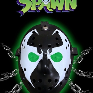 May include: A black and white hockey mask with a Spawn character design. The mask has green eyes and a black strap. The mask is surrounded by silver chains.