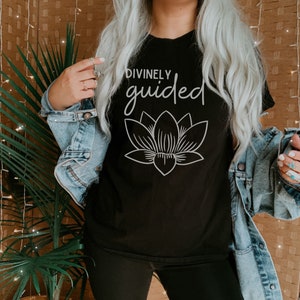 May include: Black t-shirt with the text "DIVINELY guided" and a white outline of a lotus flower.