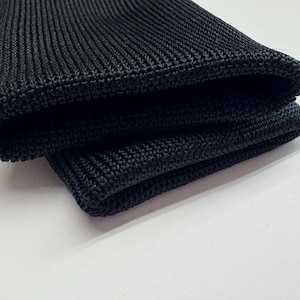 May include: Close-up of a pair of black knitted gloves. The gloves are folded over, revealing the textured knit pattern and the rounded cuff. The gloves are made of a dark, solid black material.