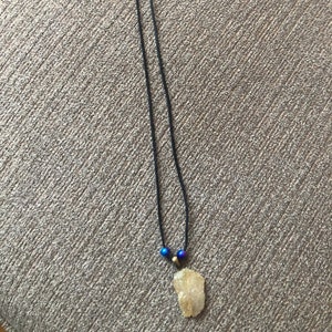 May include: A necklace with a raw quartz crystal pendant and two blue beads. The necklace is made with black cord and a silver clasp.
