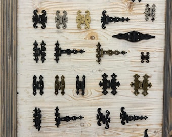 May include: A variety of decorative hinges in black, gold, and silver finishes are displayed on a light wood background. The hinges are in various styles and sizes, with some featuring ornate designs.