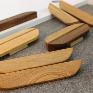 Op de afbeelding: Assortiment van houten deurknoppen voor kasten in verschillende vormen en maten. Sommige zijn ovaal, andere rechthoekig en weer andere gebogen. De knoppen zijn gemaakt van licht en donker hout.