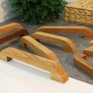 May include: Assortment of wooden cabinet drawer pulls in various shades of brown. The pulls are all different shapes and sizes, with some having a more rounded shape and others having a more rectangular shape.