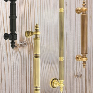 May include: Four door handles, two are gold and two are black. The handles are long and have a decorative design. They are mounted on a white wooden surface.