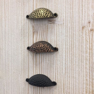 May include: Five different cabinet pulls with a hammered finish. The pulls are in a variety of colors, including gold, copper, black, and silver.