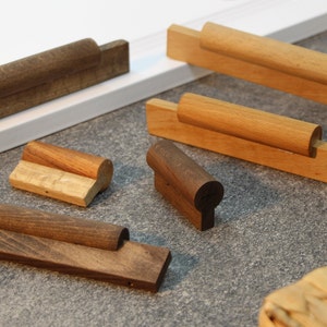 Op de afbeelding: Assortiment van houten deurknoppen voor kasten in verschillende maten en stijlen. Sommige zijn donkerbruin en andere lichtbruin. De knoppen zijn gemaakt van massief hout en hebben een afgeronde vorm.