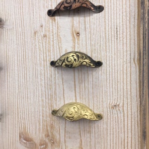 May include: Four ornate metal drawer pulls with a decorative floral design. The pulls are in various finishes, including copper, brass, and gold.