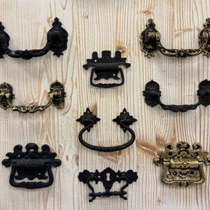 May include: Assortment of ten antique-style cabinet door pulls in black and gold finishes. The pulls are made of metal and have intricate designs.
