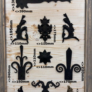 May include: Assortment of black metal decorative hinges and accents in various sizes and styles. The hinges are displayed on a wooden background with measurements in inches.
