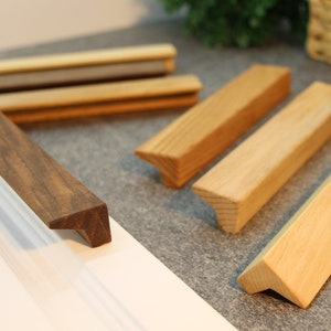 Op de afbeelding: Assortiment van houten kastgrepen in verschillende tinten bruin en natuurlijk hout. De grepen hebben een eenvoudige, rechthoekige vorm met een licht afgeschuinde rand.