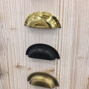 May include: Five different cabinet pulls in various finishes. The pulls are all the same shape, a half-circle with a slight curve at the top. The finishes are copper, brass, black, antique brass, and nickel.