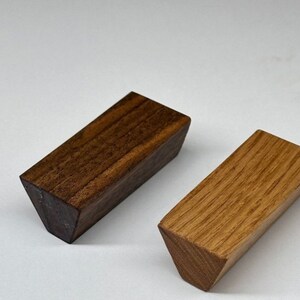 May include: Two wooden drawer pulls, one is a dark brown wood and the other is a light brown wood. Both pulls are triangular shaped.