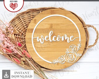 May include: A round wooden sign with the word "welcome" in a white cursive font. The sign is decorated with a white floral design and a circle around the word "welcome".