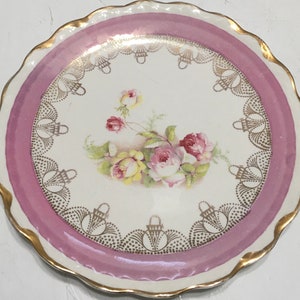 May include: A vintage porcelain plate with a pink rim and gold trim. The center features a floral design with pink and yellow roses.