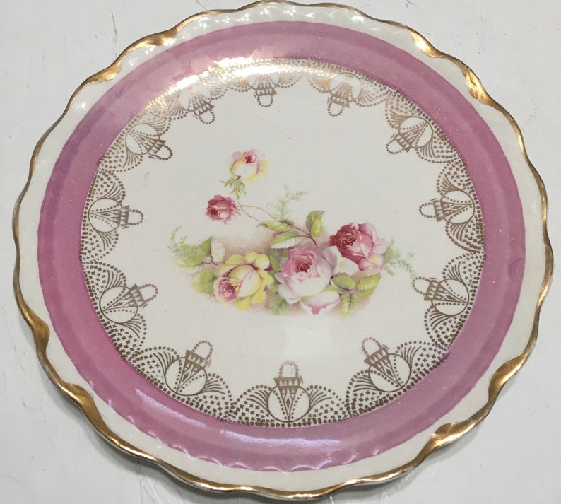 May include: A vintage porcelain plate with a pink rim and gold trim. The center features a floral design with pink and yellow roses.