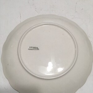 May include: White ceramic plate with a scalloped edge. The plate has a floral design and the text "D.R. Miller, Clarksburg, W.Va." printed on the bottom.