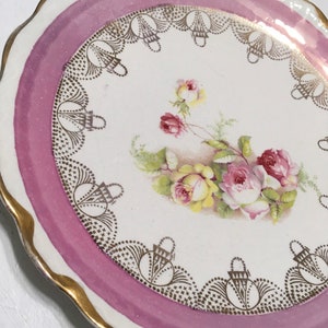 May include: A white porcelain plate with a pink rim and gold trim. The plate features a floral design with pink and yellow roses and gold accents.