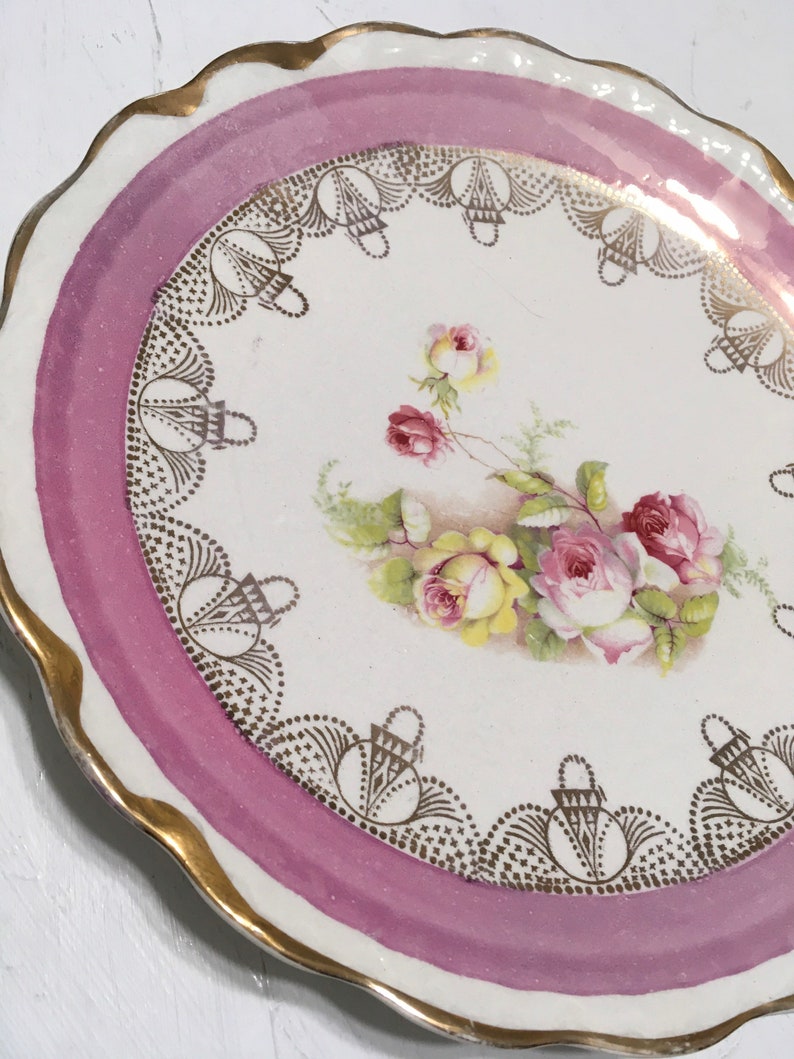 May include: A white porcelain plate with a pink rim and gold trim. The plate features a floral design with pink and yellow roses and gold accents.