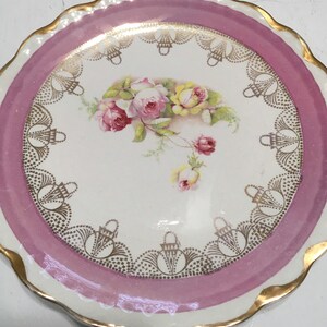 May include: A white porcelain plate with a pink rim and gold trim. The plate features a floral design with pink and yellow roses.