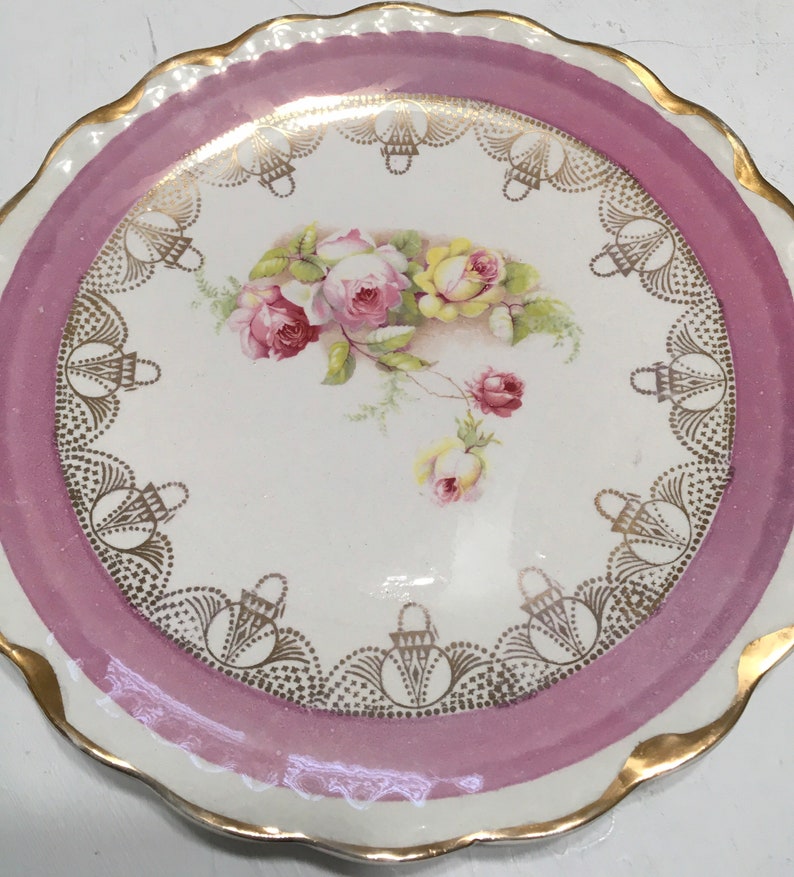May include: A white porcelain plate with a pink rim and gold trim. The plate features a floral design with pink and yellow roses.