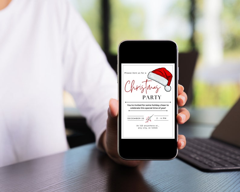 May include: A smartphone displaying a Christmas party invitation with a red Santa hat graphic. The invitation text reads "Please join us for a Christmas Party. You're invited for some holiday cheer to celebrate this special time of year! December 25, 2-4 PM, At 123 anywhere st, any city, st 12345."