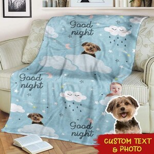 May include: A blue fleece blanket with a repeating pattern of clouds, stars, and the text "Good night". There are two images of dogs on the blanket, one with a baby's face superimposed on it.
