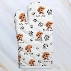 May include: White oven mitt with a quilted pattern featuring a repeated design of a brown dog with the text "DOG MOM" and black paw prints.