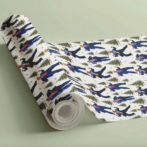 May include: A roll of white wrapping paper with a repeating pattern of figures in blue suits carrying Christmas trees. The design includes small gold stars and green Christmas trees. The paper is rolled up, showing the pattern.