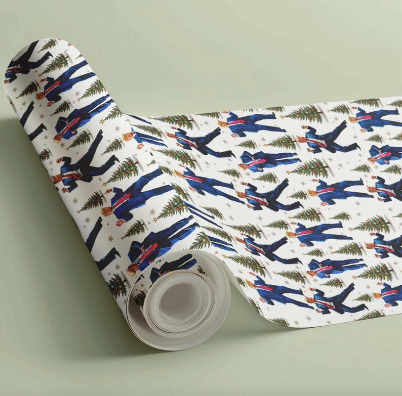 May include: A roll of white wrapping paper with a repeating pattern of figures in blue suits carrying Christmas trees. The design includes small gold stars and green Christmas trees. The paper is rolled up, showing the pattern.