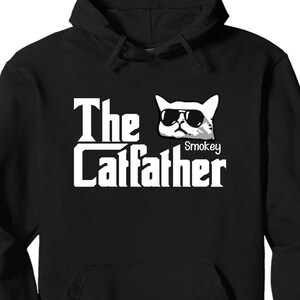 May include: Black hooded sweatshirt with a white graphic of a cat wearing sunglasses and the text "The Catfather" with the name "Smokey" under the cat.